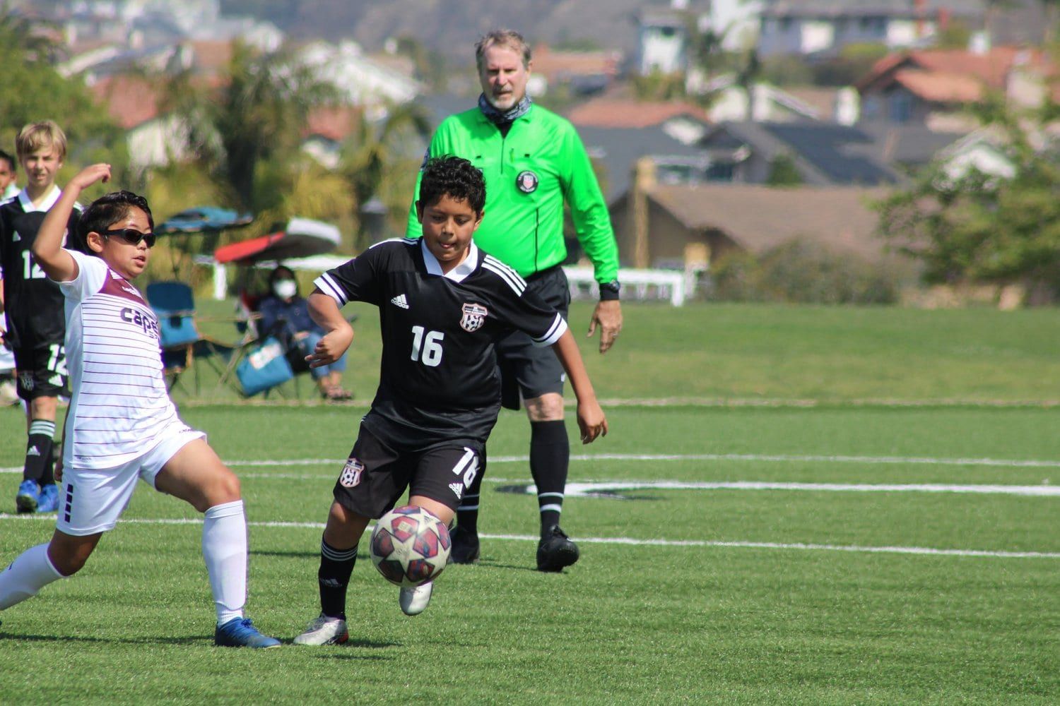 Boys player in black dribbling past a defender as the referee follows play