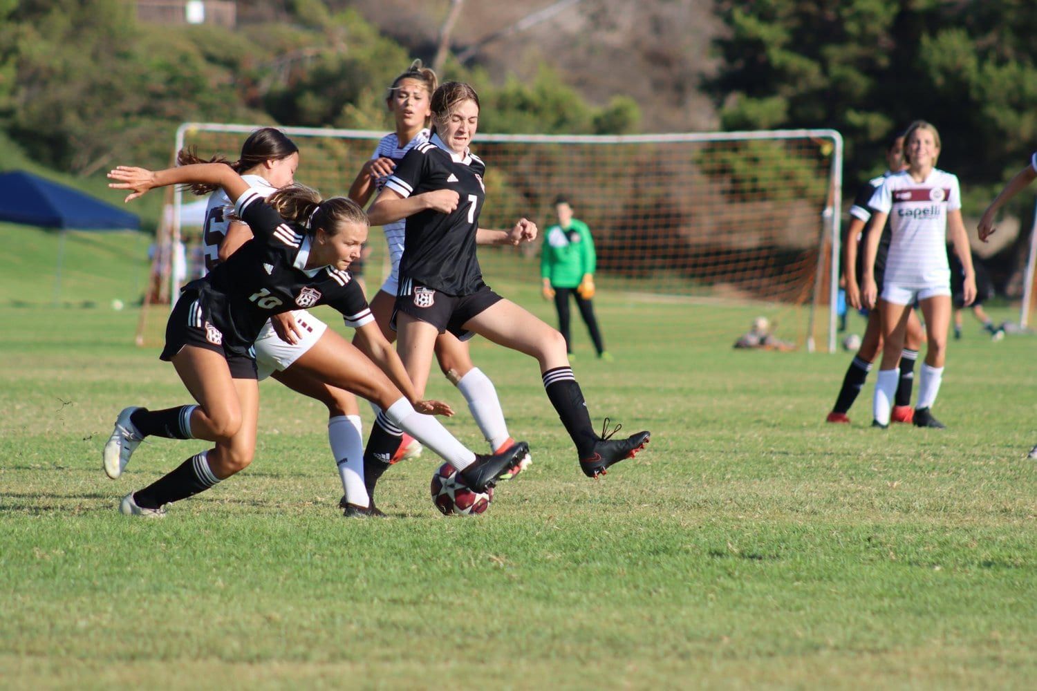 Girls in black racing for the ball in an Aliso Cup match